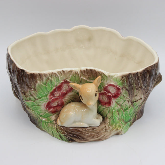 A ceramic woodland-themed planter shaped like a tree trunk, featuring a small beige deer figurine at the center, green leaves, and red berries around the base, set against a plain light gray background.