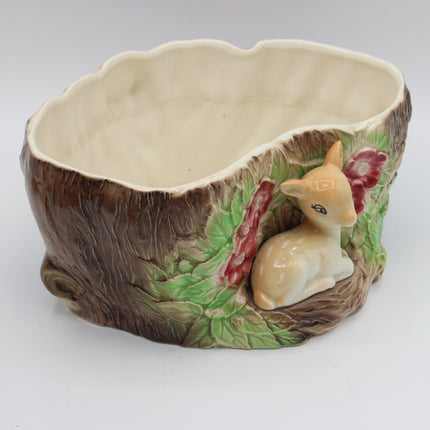 A ceramic woodland-themed planter shaped like a tree trunk with a small deer figurine and green leaves on the front, photographed on a plain light background.