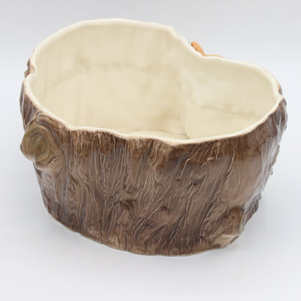 A ceramic planter shaped like a tree trunk, featuring a textured brown bark exterior and a smooth, cream-colored glazed interior, shown on a plain white background.