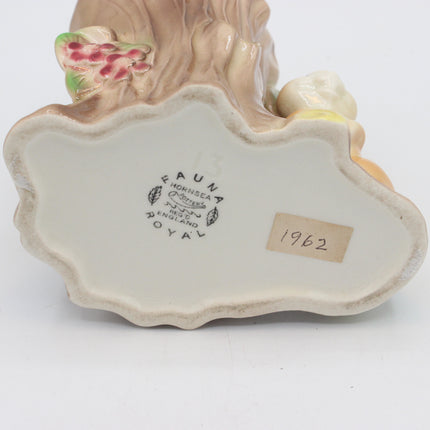 Close-up of the base of a vintage ceramic figurine, showing the interior stamp 'Royal Dornheide Germany 1962' and a paper sticker with '1962'. The base is cream-colored with a hand-painted brown tree trunk and small green and pink berry accents.