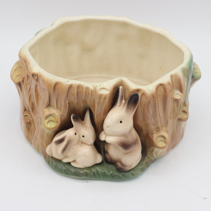 A ceramic rabbit-themed bowl shaped like a tree stump, featuring two small rabbit figurines nestled in the base on a white background.