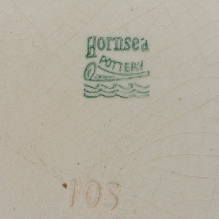 The underside of a ceramic plate or dish showing a cream-colored glaze with fine crackle lines, a green 'Hornsea Pottery' mark, a handwritten paper label on the left, and the number '105' stamped below.