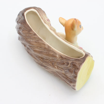 A ceramic log-shaped planter with a small deer figurine peeking out from the top, set against a plain white background.
