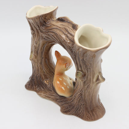 A ceramic double-vase figurine shaped like a tree stump with a small fawn sitting inside the center, on a white background.