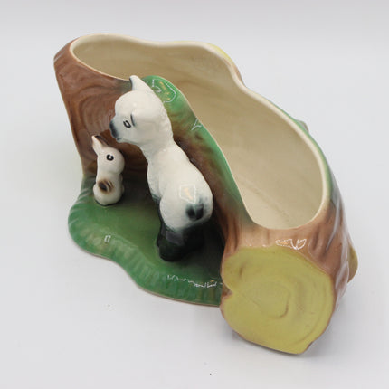 A ceramic planter shaped like a tree trunk with two painted alpacas standing on a green base, photographed on a plain white background.