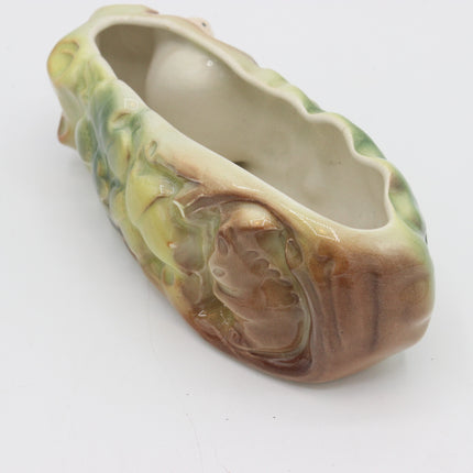 An antique ceramic planter shaped like a stylized leaf or acanthus leaf, featuring a glossy glaze with green, yellow, and brown tones over an off-white base, photographed on a white background.