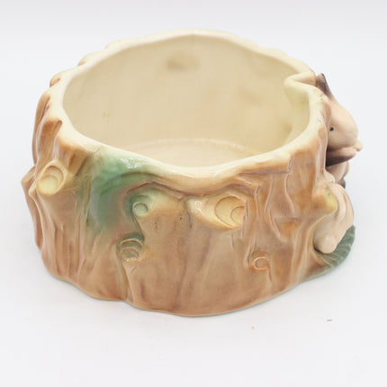 A ceramic rabbit-shaped bowl designed to look like a tree stump, featuring a light beige interior, a brown textured exterior with green glaze accents, and a small rabbit figure peeking out from the right side.