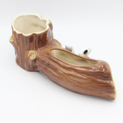 A ceramic planter shaped like a tree stump, featuring a glossy brown textured exterior and a light beige interior, with small white and black animal figurines peeking out from the side on a white background.