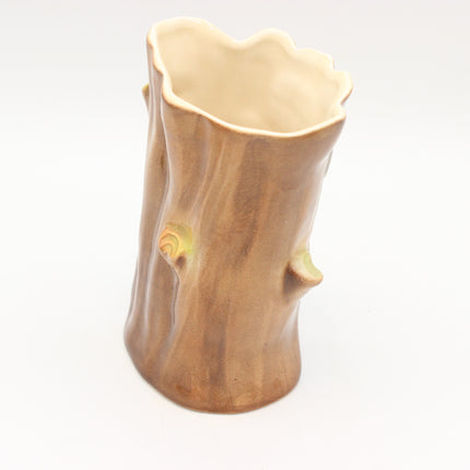 A ceramic pot shaped like a tree trunk with a rustic bark texture, featuring a scalloped rim and small branch details, set against a plain white background.