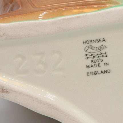 Close-up of the underside of a ceramic object, showing the brand mark 'HORNSEA' and registration details, with a cream-colored base, a brown glazed section, and a green glazed edge.