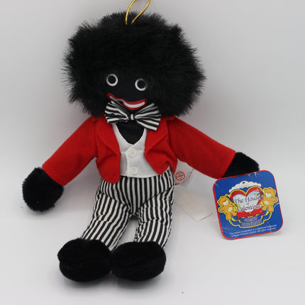 A plush toy of The Jolly Golliwog from 'The Jolly Golliwog Show', featuring black fur, a red jacket, white shirt, black and white striped bow tie and trousers, and a gold hanging loop, shown with its original blue packaging tag on a white background.