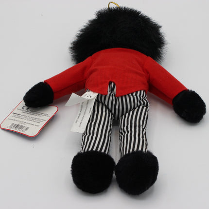 A small plush toy Golly shown from the back on a plain white background, wearing a bright red top, black-and-white vertically striped pants, black fluffy cuffs and head, with a hang tag attached.