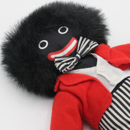 A novelty Golly doll with black fur, a black and white striped bow tie, a red jacket, and a white shirt with black and white striped pants, shown on a plain white background.