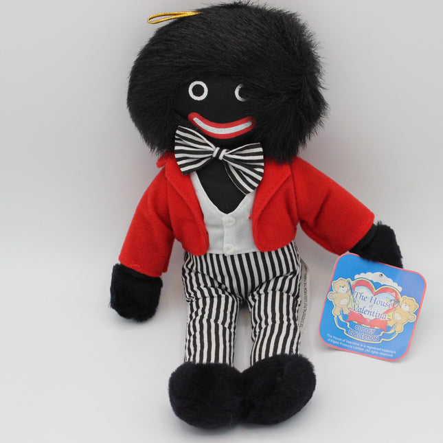 A plush toy Golly doll with black hair, a red jacket, black-and-white striped bow tie and pants, and a white shirt, posed against a light gray background with a blue 'The House of Valentine' tag attached.