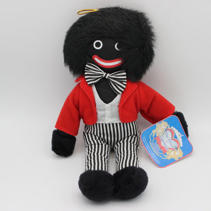 A plush toy doll with black hair and a black face, wearing a red jacket, white shirt, black-and-white striped bow tie and striped pants, sitting on a light gray background with a blue hangtag attached.
