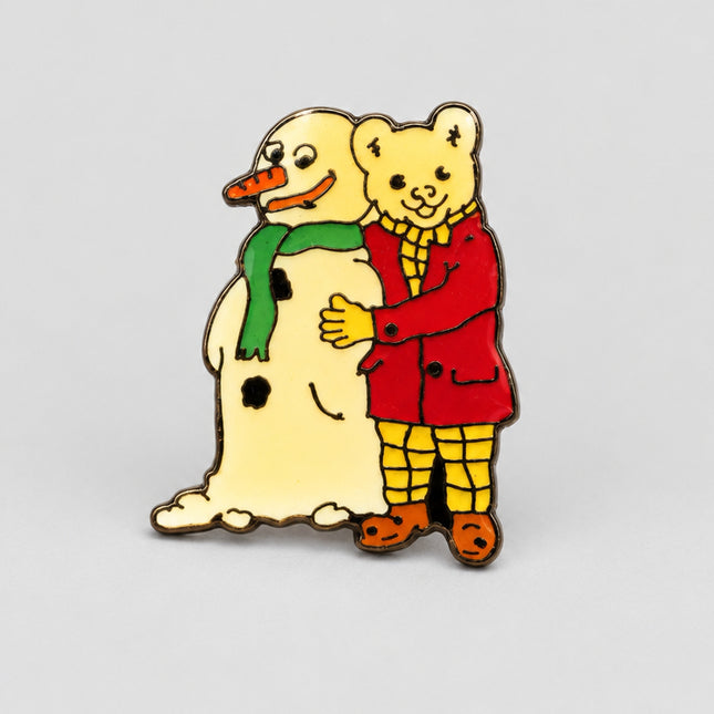 A small enamel pin depicting a yellow bear hugging a snowman, shown on a plain white background.