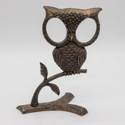 A dark metal owl-shaped wall hook or decorative stand, mounted on a branch-like base, photographed against a plain light gray studio background.