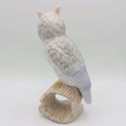 A ceramic owl figurine perched on a branch, shown from the back against a plain light gray background.