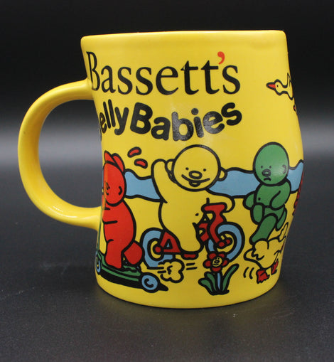 Yellow mug with cartoon characters and 'Bassetts Jelly Babies' text on a dark background