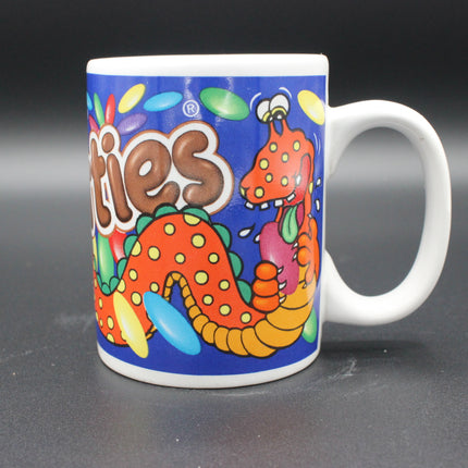Colorful mug with cartoon characters and 'Smarties' branding on a dark background