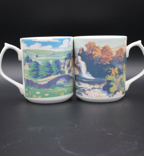 Two mugs with scenic designs on a dark background