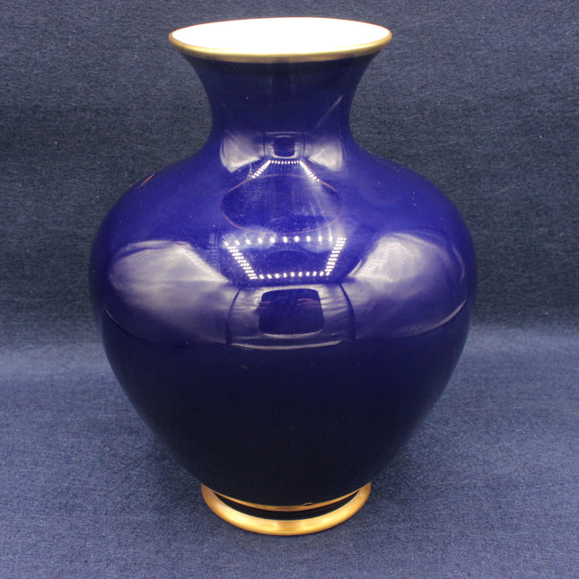 Blue ceramic vase with gold base and rim on a dark blue background