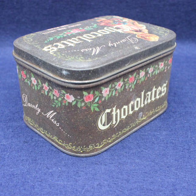 Decorative tin box with 'Dainty Miss Chocolates' text on a blue background
