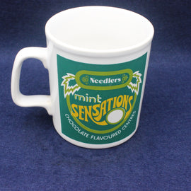White mug with green and yellow 'Needlers Mint Sensations' design on a blue background