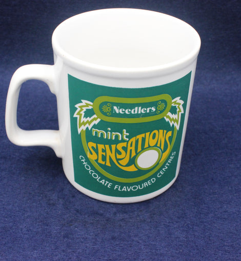 White mug with green and yellow 'Needlers Mint Sensations' design on a blue background