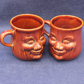 Two brown ceramic mugs with face designs on a blue background