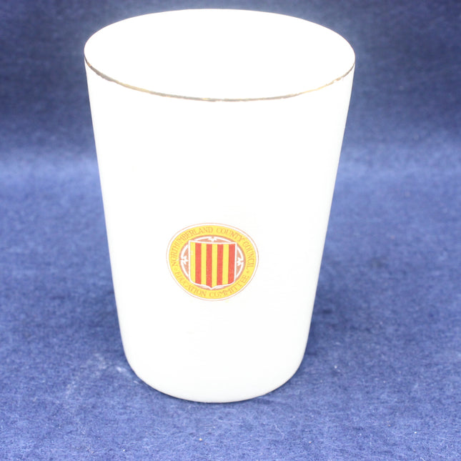 White ceramic tumbler with a yellow and red emblem on a blue background