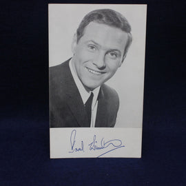 Black and white photo of a smiling man with a signature on a dark background