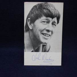 Black and white photo of a smiling John Noakes with a signature below on a dark background