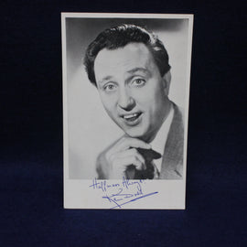 Black and white photo of a Ken Dodd with a signature below on a dark background
