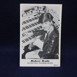 Black and white photo of a man playing an organ with text 'Robert Wolfe International Recording Artist' on a dark background