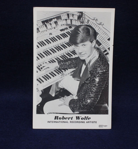 Black and white photo of a man playing an organ with text 'Robert Wolfe International Recording Artist' on a dark background