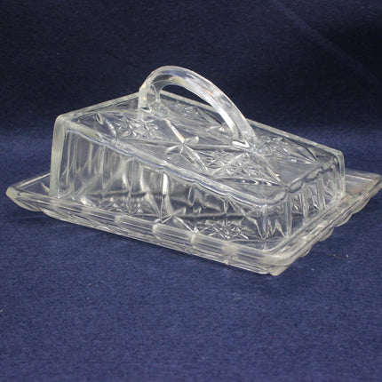 Clear glass butter dish with lid on a blue background