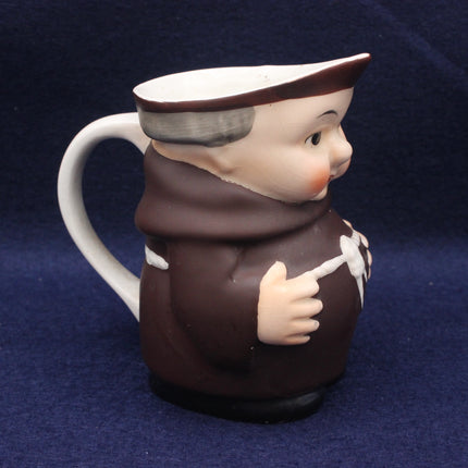 Ceramic pitcher shaped like a monk with a white handle on a dark blue background