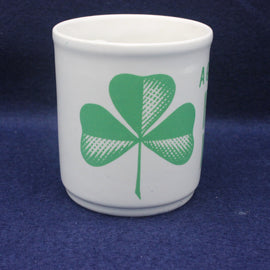 White cup with green four-leaf clover design on a blue background