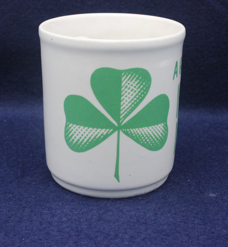 White cup with green four-leaf clover design on a blue background