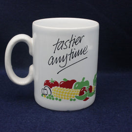 White mug with 'tastier anytime' text and vegetable graphics on a dark background