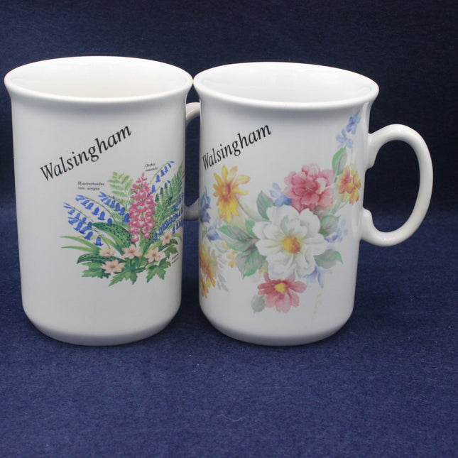 Two white mugs with floral designs and 'Walsingham' text on a blue background
