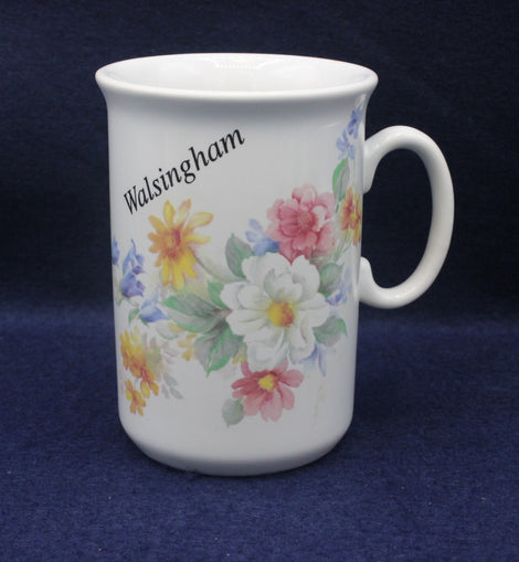 White mug with floral design and 'Walsingham' text on a dark blue background