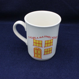White mug with yellow house design and red text on a dark blue background