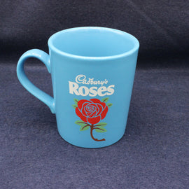 Blue mug with 'Cadbury's Roses' branding on a dark background