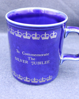 Blue mug with white text and crowns, commemorating the Silver Jubilee, on a gray background
