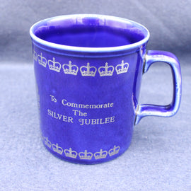 Blue mug with white text and crowns, commemorating the Silver Jubilee, on a gray background