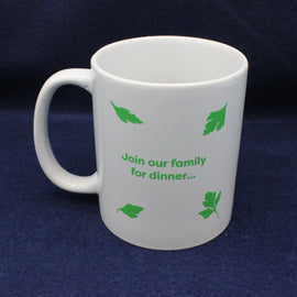 White mug with green text and leaf patterns on a dark blue background