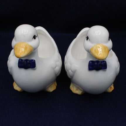 Two ceramic duck figurines with bow ties on a dark background