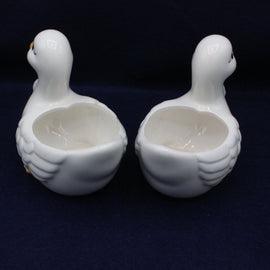 Two white ceramic duck-shaped bowls on a dark background